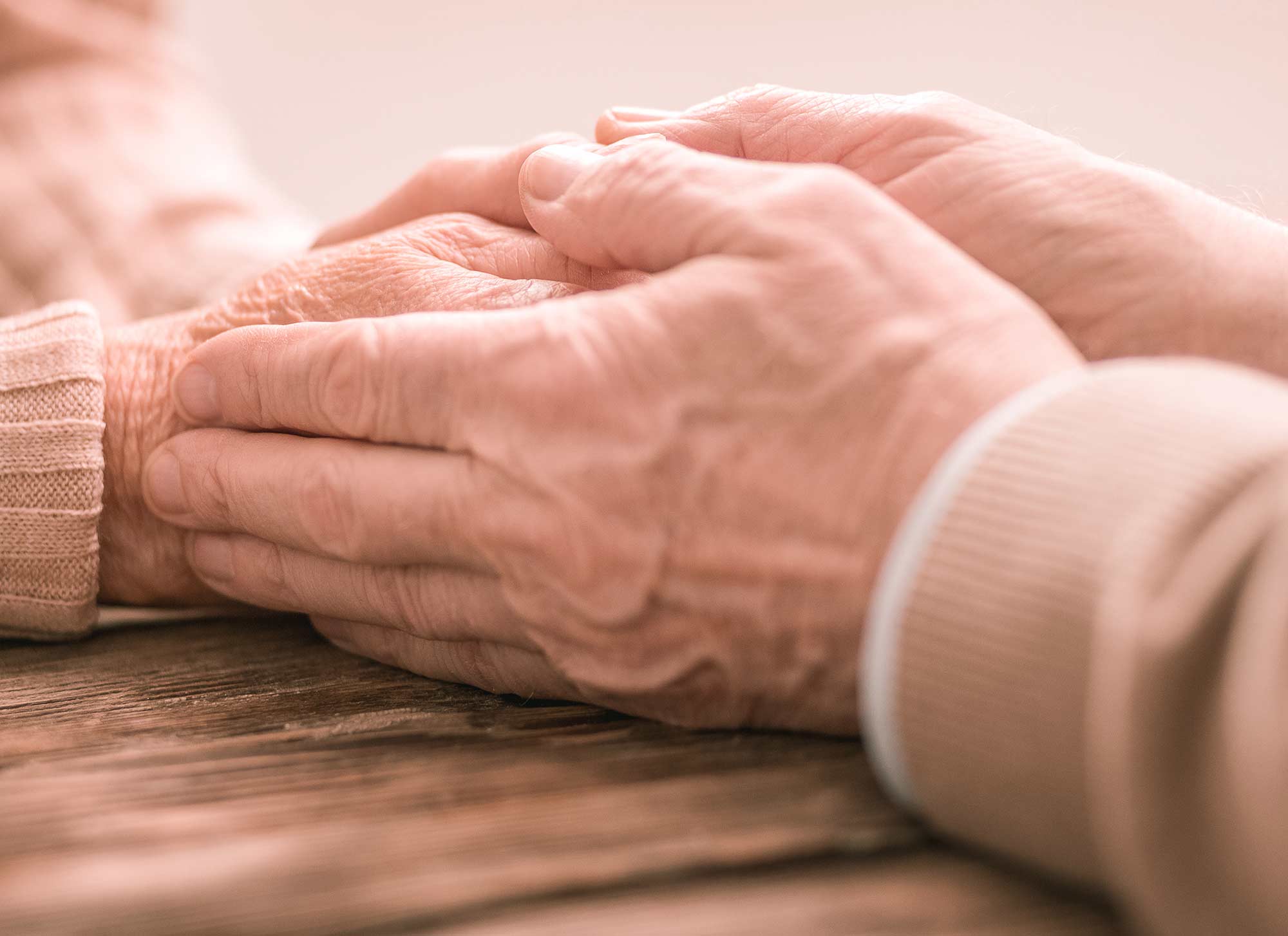Eine jüngere Hand hält behutsam die Hände eines älteren Menschen – Sinnbild für Fürsorge und Begleitung.