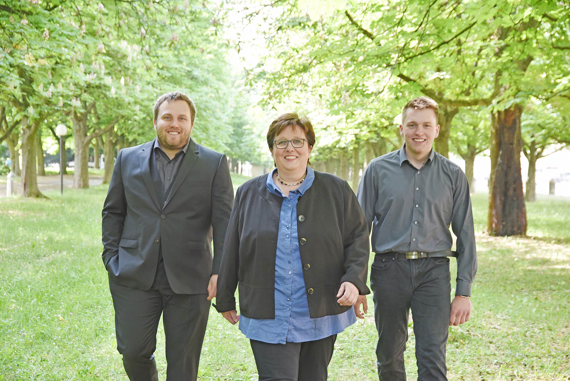 Das Team von Junge Bestattungen – drei Personen in einer ruhigen, baumbestandenen Allee.
